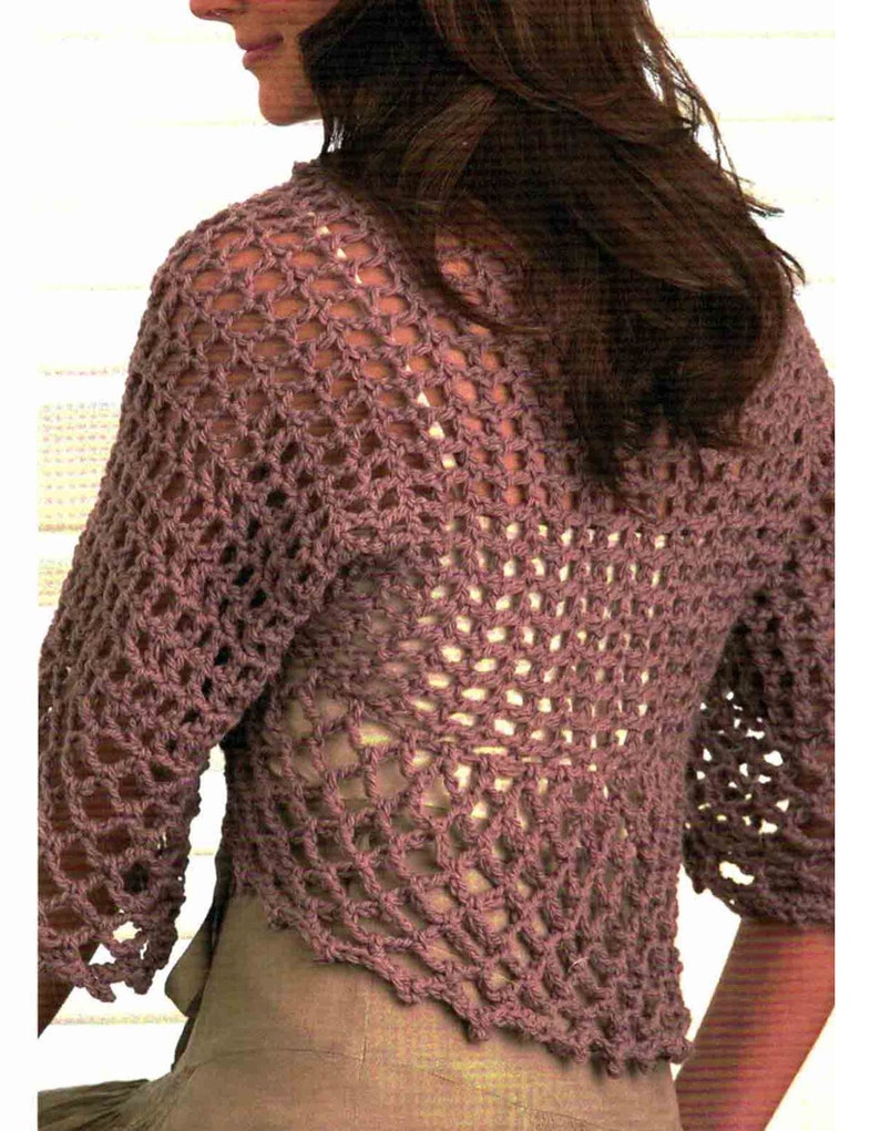 May include: A mauve crocheted shrug with a lacy openwork design. The shrug has a V-shaped neckline and three-quarter sleeves.