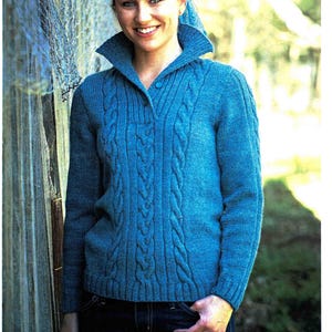 May include: A teal blue cable-knit jumper with a collared neckline and button closure. The jumper features a textured cable design down the front and on the sleeves. The model is wearing the jumper with dark blue jeans.