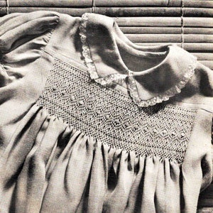 May include: A white baby dress with a smocked bodice and a lace collar. The dress is made of a soft, lightweight fabric and is perfect for a special occasion.