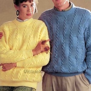 Könnte beinhalten: Zwei Pullover mit Zopfmuster, einer gelb und einer blau, mit einem ähnlichen Muster. Die Pullover werden von zwei Personen getragen, eine steht hinter der anderen.