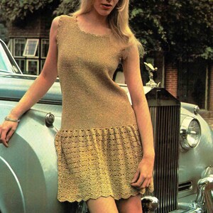 May include: A sleeveless gold-toned knit dress featuring a fitted bodice and a flared skirt with a scalloped hemline. The garment is constructed with a fine, textured stitch pattern throughout, transitioning into a decorative shell-like design.
