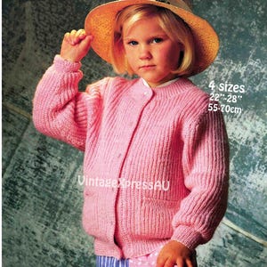 May include: A pink knitted cardigan with a button-up front and two front pockets. The image also includes text that reads "4 sizes 22"-28" 55-70cm". The cardigan is worn with a straw hat.