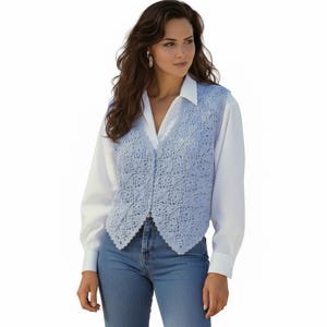 May include: A light blue crochet vest featuring a repeating floral motif pattern with a V-neckline and a button-front closure, layered over a crisp white long-sleeved collared shirt and paired with classic blue denim jeans.