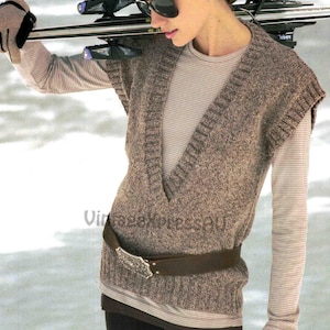 May include: A brown knitted vest with a deep V-neck, worn over a striped long-sleeved top. A brown leather belt with a decorative silver buckle cinches the waist. The person is wearing sunglasses and carrying skis.
