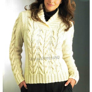 May include: A cream-colored cable knit sweater with a wide, folded collar. The sweater has a detailed cable knit pattern and long sleeves.