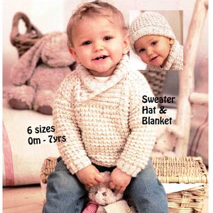 May include: A child wearing a cream-colored knit sweater and jeans, sitting in a wicker basket. The image includes a smaller inset of a child wearing a matching knit hat. Text reads "Sweater, Hat & Blanket" and "6 sizes 0m - 7yrs."