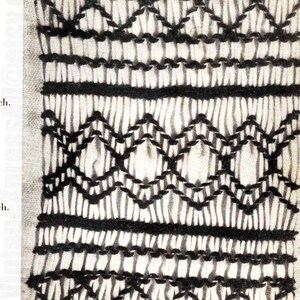 May include: A close-up of a white fabric with black embroidery. The embroidery is in a repeating pattern of diamonds and lines.