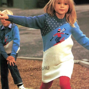 May include: Two children wearing matching blue and white knit sweaters with a skier design. The sweaters have a diagonal color block design with a skier graphic. The girl is wearing a white knit dress and red tights.