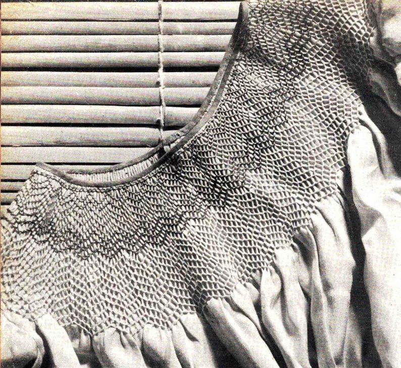 May include: A close-up of a white smocked fabric with a detailed pattern. The fabric is folded and draped over a wooden slatted blind.