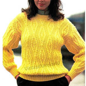 May include: A yellow knitted sweater with a cable knit pattern. The sweater has a round neckline and long sleeves.