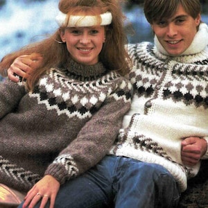 May include: Two people wearing matching patterned sweaters. One sweater is brown with white and black accents, the other is white with brown and black accents. Both sweaters have a high neck and are buttoned.