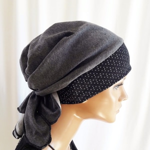 Op de afbeelding: Een grijze hoofdbedekking met een gelaagd ontwerp. De bovenste laag is een effen grijze stof, terwijl de onderste laag zwart is met kleine witte stippen. De hoofdbedekking is aan de achterkant vastgebonden met een strik.