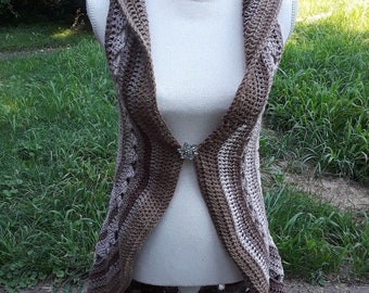 May include: A brown and beige crocheted vest with a hood and a decorative button closure. The vest has a long, flowing design and is made with a textured stitch.