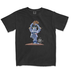 May include: Black t-shirt with a cartoon illustration of a baseball player wearing a blue and white uniform, holding a baseball glove and a baseball. The player is standing on a dirt mound. The text "Dodgers 34" is on the player's uniform.