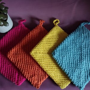 Può includere: Quattro presine all'uncinetto in diversi colori: rosa, arancio, giallo e blu. Le presine sono realizzate con un semplice motivo a punto e hanno una forma quadrata.