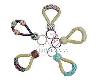 Könnte beinhalten: Fünf Schlüsselanhänger aus geflochtenem Seil mit verschiedenen farbigen Akzenten. Jeder Schlüsselanhänger hat einen Metallring zum Anbringen von Schlüsseln. Die Schlüsselanhänger sind eine Mischung aus Braun, Rot, Schwarz, Weiß und Blau.