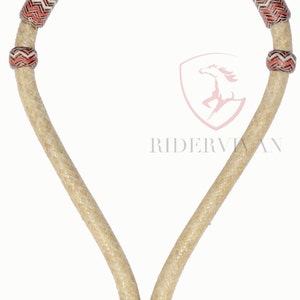 Puede incluir: Un cabezada de cuero trenzado para caballo con un patrón de chevron rojo y blanco. La cabezada tiene un solo nudo en la parte inferior.
