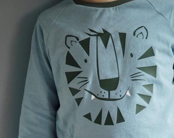 May include: A light blue long-sleeved shirt with a green tiger face graphic. The shirt has a green trim around the neck and cuffs.