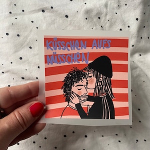 Könnte beinhalten: Ein Sticker mit rotem und weißem gestreiftem Hintergrund. Der Sticker zeigt eine schwarz-weiße Illustration von zwei Personen, die sich umarmen. Der Text "KÜSSCHEN AUFS NÜSSCHEN" ist in Lila auf dem Sticker geschrieben.