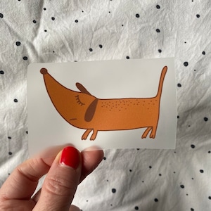 May include: A brown dachshund with closed eyes and a long snout is depicted in a cartoon style on a white background. The dachshund is facing to the right and has a spotted pattern on its body.
