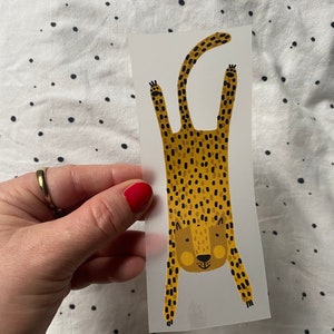 Könnte beinhalten: Ein transparenter Aufkleber mit einer Cartoon-Illustration eines kopfüber hängenden Leoparden. Der Leopard ist gelb mit schwarzen Flecken und hat einen freundlichen Ausdruck.