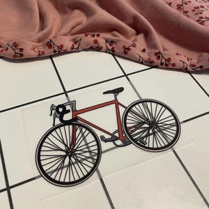 Peut inclure: Un vélo rouge avec des roues noires et un guidon noir. Le vélo est sur une surface carrelée blanche.