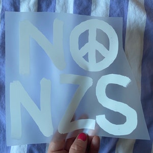 Peut inclure: Un signe de paix blanc et les lettres "NO NZS" sont imprimés sur une feuille de plastique transparente.