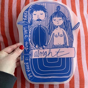 Könnte beinhalten: Blaue und weiße Illustration von zwei Meerjungfrauen, die sich an den Händen halten, mit dem Wort "alright" in einem Banner. Der Satz "every little thing is gonna be" steht vertikal an der Seite. Das Kunstwerk befindet sich auf einem transparenten, flexiblen Material.