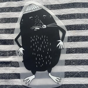 Könnte beinhalten: Ein schwarz-weißer Aufkleber mit einem Cartoon-Maulwurf, der eine gestreifte Mütze trägt. Der Maulwurf hat weiße Schnurrhaare, einen weißen Bauch und weiße Hände und Füße. Der Aufkleber befindet sich auf einem gestreiften Hintergrund.
