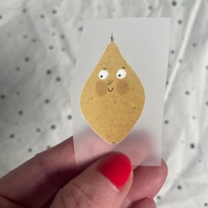 Op de afbeelding: Een gele citroensticker met een cartoon gezicht, witte ogen en een kleine glimlach. De sticker zit op een doorzichtig vel.