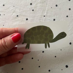 Könnte beinhalten: Ein grüner Schildkrötenaufkleber mit einem gemusterten Panzer. Die Schildkröte lächelt und hat einen langen Hals.