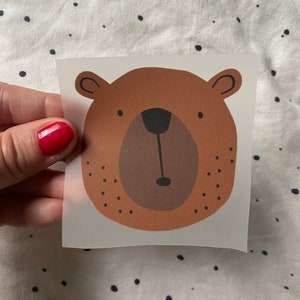 Könnte beinhalten: Ein braunes Bären Gesicht mit einer schwarzen Nase und Augen. Der Bär ist auf einem klaren Hintergrund.