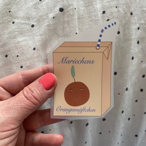 Könnte beinhalten: Ein Aufkleber mit einem Cartoon-Orangensaftkarton mit einem Strohhalm. Der Karton ist mit "Mariecchens Orangensäftichen" beschriftet.