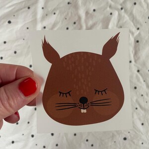 Könnte beinhalten: Ein braunes Cartoon-Eichhörnchen mit geschlossenen Augen und einem kleinen Lächeln. Das Eichhörnchen hat eine schwarze Nase und Schnurrhaare.