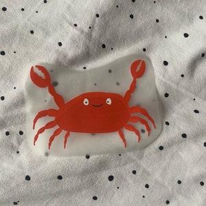 Op de afbeelding: Een rode krab met een glimlach op een doorzichtige sticker.