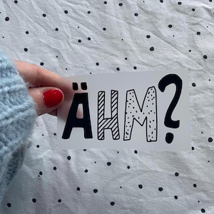 Könnte beinhalten: Ein weißer Aufkleber mit schwarzer Schrift, auf dem in einem verspielten, handgezeichneten Stil "ÄHM?" steht.