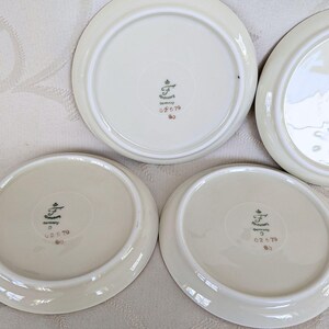 May include: Four off-white porcelain plates with a slightly raised rim. The underside of each plate features a central emblem with text that reads "F" and "Germany". The plates are arranged on a light-colored surface.
