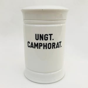 Könnte beinhalten: Weiße Keramikdose mit schwarzem Deckel und schwarzer Aufschrift "UNGT. CAMPHORAT."