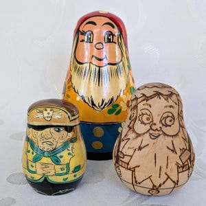 Könnte beinhalten: Drei farbenfrohe russische Matrjoschka-Puppen. Die größte Puppe hat einen roten Hut und einen langen weißen Bart. Die mittlere Puppe ist gelb und blau. Die kleinste Puppe trägt einen braunen Hut und eine gelbe Jacke.