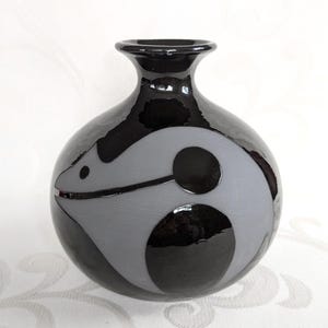 Könnte beinhalten: Eine schwarze Keramikvase mit einem grauen abstrakten Design. Die Vase hat einen runden Körper und einen schmalen Hals.
