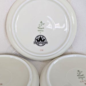 May include: A set of three off-white ceramic plates. Each plate has a raised rim and a central design featuring the text "STAFFELKLEMMEN" and "Germany". The number "24" is printed in red on one plate.