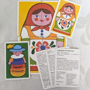 Può includere: Un gioco di puzzle per bambini con illustrazioni colorate di bambole Matrioska e altri personaggi. Il gioco include carte con immagini e testo, progettate per far assemblare e imparare i bambini piccoli. Il gioco è progettato per scopi educativi.