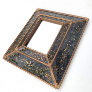 May include: A small square mirror with a decorative wooden frame. The frame is painted with gold and blue floral patterns.