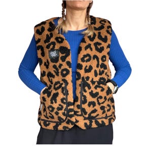 Könnte beinhalten: Eine braun-schwarze Weste mit Leopardenmuster, zwei Vordertaschen und schwarzem Besatz. Die Weste hat eine weiche, flauschige Textur und einen kleinen Aufnäher mit Text auf der oberen linken Brust. Die Person trägt ein blaues Langarmshirt.