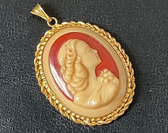 May include: Gold tone pendant with a cameo of a woman's profile in cream and red.