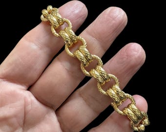 May include: A gold chain bracelet with a textured, rope-like design. The bracelet is made of multiple linked circles.
