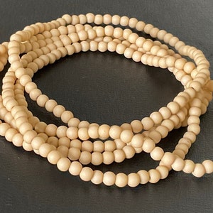 Op de afbeelding: Een streng natuurlijke houten kralen in een licht beige kleur. De kralen zijn rond en glad en aan elkaar geregen op een doorzichtige draad. De kralen zijn in een losse spiraal gerangschikt.