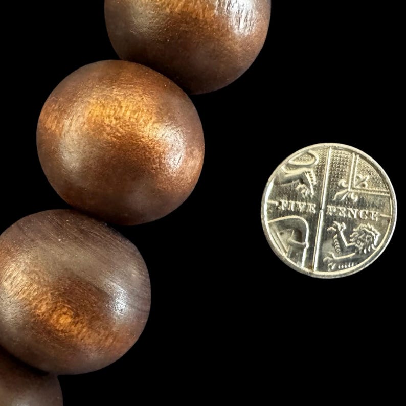 May include: Close-up of large, round, wooden beads with a warm brown finish. A silver Five Pence coin is next to the beads. The beads have a smooth, polished appearance, and the coin shows intricate details.