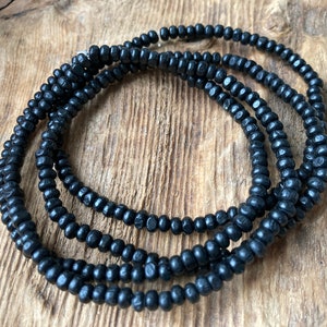 May include: A strand of black wooden beads, arranged in a circular shape on a wooden surface.