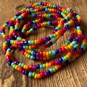 May include: A multi-coloured beaded necklace with rainbow colours, including red, orange, yellow, green, blue, indigo, and violet. The beads are strung together in a circular pattern, creating a layered effect.